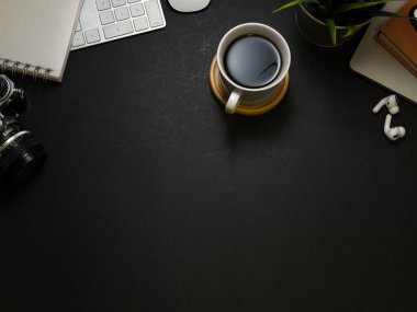 Kahve fincanı, kırtasiye malzemesi, kulaklık ve fotokopi alanı olan karanlık çalışma alanının en üst görüntüsü.