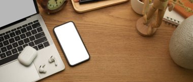 Akıllı telefon, dizüstü bilgisayar, kulaklık ve ahşap masa dekorasyonlu ev ofis masasının en üst görüntüsü.