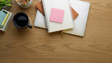 Not defteri, kahve fincanı, dizüstü bilgisayar, kırtasiye ve kopyalama alanı olan çalışma tablosunun üst görünümü