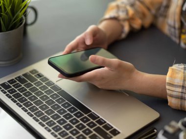 Akıllı telefon ve dizüstü bilgisayarla çalışan serbest çalışan kadın ofis odasındaki çalışma alanını kapatın.