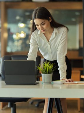 İş yerinde duran ve ofis masasında dijital tabletle çalışan kadın ofis çalışanının portresi.