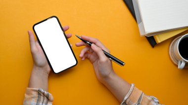 Akıllı telefon ile çalışan ve elinde kalemle şık bir çalışma alanında çalışan serbest çalışan bayan çalışanın en iyi görüntüsü.