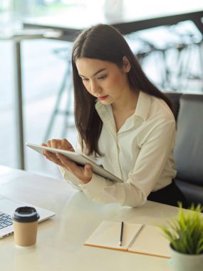 Portrait of busy female office worker concentrating on her work with digital tablet in her hand 