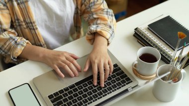 Scott ceketli kadın serbest çalışanın ofis masasında kahve fincanı ile dizüstü bilgisayarda daktilo kullanmasını yakından izle.