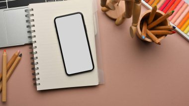 Akıllı telefon, defter, boya araçları ve ev ofisinde dizüstü bilgisayarı olan kadınsı çalışma alanı, kırpma yolu