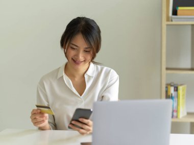 Akıllı telefondan alışveriş yapan ve elinde banka kartı tutan gülümseyen bir kadının portresi.