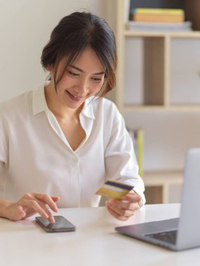 Akıllı telefondan alışveriş yapan mutlu kadın portresi ve oturma odasında otururken kredi kartıyla ödeme.