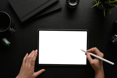 Koyu çalışma alanı üzerinde stilus kalemle dijital tablet kullanan kadın ellerinin üst görünümü, kırpma yolu