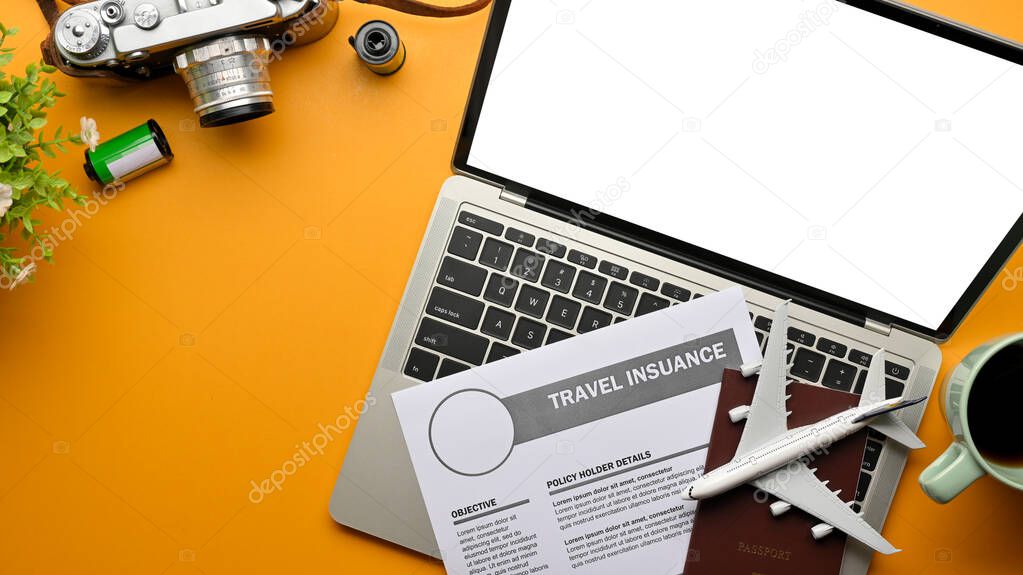 Top view of creative flat lay photo of yellow table with laptop, travel insurance form, passport, camera, and airplane model, clipping path