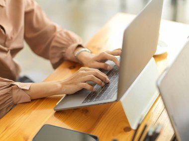 Ofis malzemeleriyle birlikte tahta ofis masasında dizüstü bilgisayarda yazan kadın işçinin yan görüntüsü