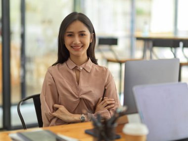 İş yerinde otururken kameraya gülümseyen genç bayan ofis çalışanının yarım boy portresi.