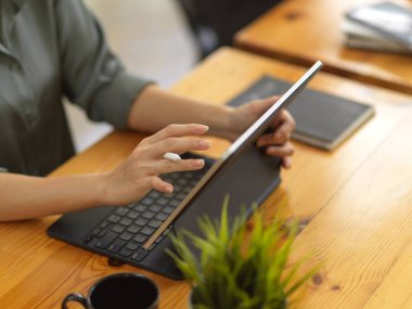 Rahat ofis odasındaki ahşap masada dijital tabletle çalışan kadın ellerinin yan görüntüsü