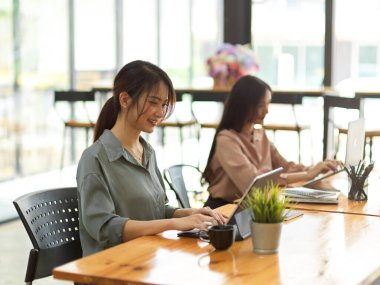 Ofis odasında yan yana otururken ofis malzemeleriyle çalışan iki kadın ofis çalışanının yan görüntüsü.