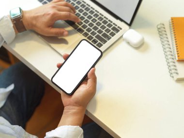 Akıllı telefon ve dizüstü bilgisayarla çalışan serbest çalışan erkek çalışanın ana ofis odasındaki beyaz masada kesme yolu.