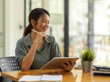 Rahat ofis odasında dijital tabletle çalışırken gülümseyen mutlu bir kadının görüntüsü.