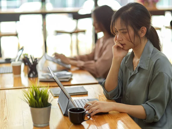 Side view of female office worker working with digital tablet in office room with her coworker