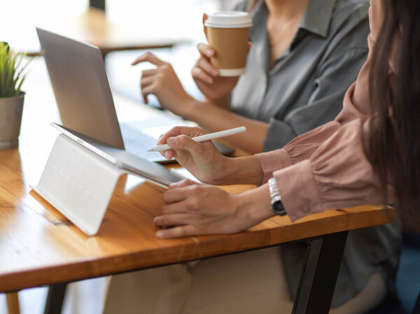 Вид сбоку двух офисных работниц, работающих с ноутбуком и планшетом в зале заседаний для реализации своего проекта