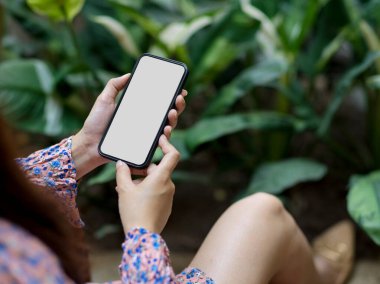 Güzel bir bahar elbisesi giymiş, akıllı telefon kullanan bir kadının kırpılmış görüntüsü evdeki bahçedeki ekran kesimini de içeriyor.