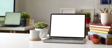 Modern ofis odası, dizüstü bilgisayarı, kırtasiyesi, bardağı ve süslemeleri masanın üzerinde.