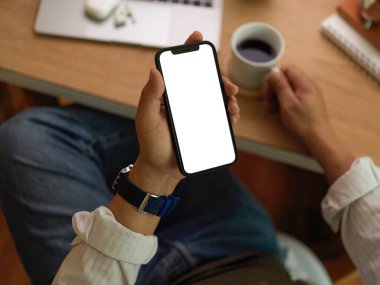 İş adamının ekranı taklit ederek akıllı telefon kullanırken ve çalışma alanında kahve fincanı tutarken, patikayı keserken.