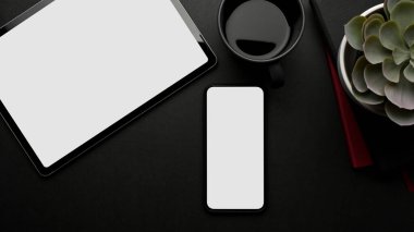 Akıllı telefonu, dijital tableti, kahve fincanı ve saksısı olan karanlık yaratıcı çalışma alanının üst görüntüsü, kırpma yolu.