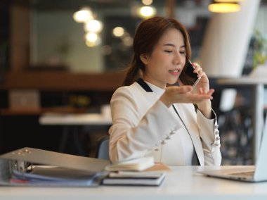 Ofiste çalışırken telefonda konuşan beyaz takım elbiseli bir iş kadınının portresi.