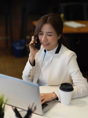 Beyaz takım elbiseli bir iş kadınının ofis odasında dizüstü bilgisayarla konuşurken çekilmiş görüntüsü.