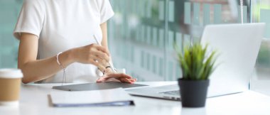 Masada dizüstü bilgisayarlı ve kütüphanede kırtasiyeli dijital tablet kullanan kadınların el resimleri.