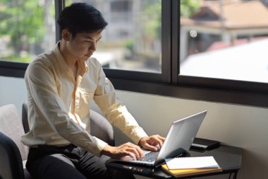 Genç ve başarılı bir işadamı ofis odasında dizüstü bilgisayar kullanırken projesinde çalışıyor.