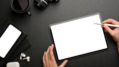 Kadın ellerinin dijital tablet kullanarak akıllı telefon, kamera ve malzemelerle karanlık yaratıcı çalışma alanı kullanmasının en üst görüntüsü, kırpma aplikasyonu