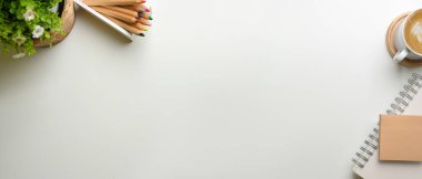 Kırtasiye malzemesi, kahve fincanı, saksı ve fotokopi alanı olan yaratıcı düz çalışma alanı beyaz masanın üzerinde.