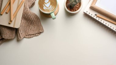Süveter, kırtasiye, kitap, kahve fincanı, kaktüs tenceresi ve fotokopi alanı olan basit çalışma masasının üst görüntüsü. 