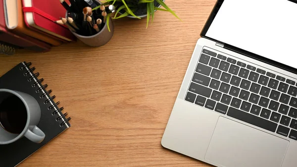 Top view of simple workspace with laptop, cup, notebook, stationery and copy space on wooden table