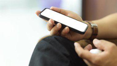 Kanepede rahatça otururken yol ekranını kırpmayı içeren akıllı telefonu tutan erkeğin yan görünümü