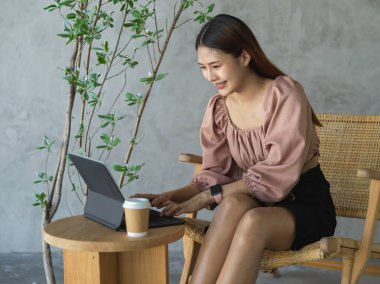 Ofisin rahat köşesinde dijital tablet ve kırtasiye malzemesi kullanan genç bir bayan işçi.