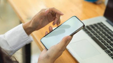 İş yerinde dizüstü bilgisayarla çalışırken akıllı telefon kullanan kadınların yan görüntüsü