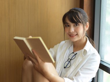 Kitap okurken kameraya gülümseyen kız öğrencinin portresi 