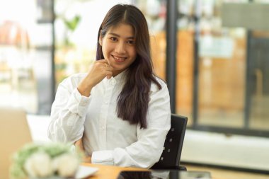 Ofiste otururken kameraya gülümseyen kadın ofis çalışanının portresi.