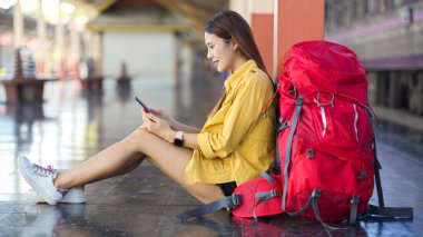 Trenin durması için platformun zemininde otururken dijital tablet kullanan kadın yolcuların yan görüntüsü 