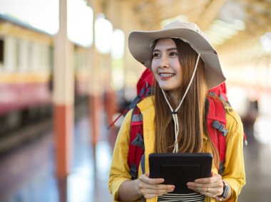 Tren istasyonunda çalışırken dijital tablet taşıyan mutlu genç bayan sırt çantasının portresi