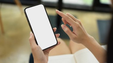 Close up view of female using smartphone with mock-up screen while sitting in workplace