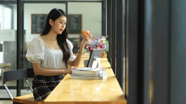 Young Pretty Female Student Holding Apple While Doing Homework Digital — Fotografia de Stock