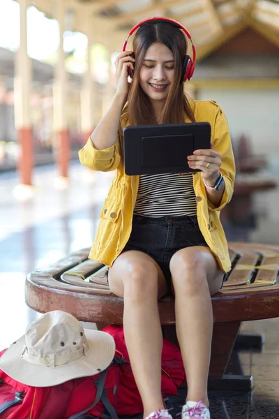 Portrait of female backpacker using digital tablet and headphone while waiting the train in platform