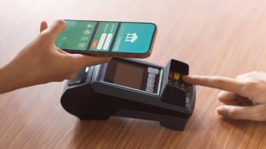 Müşteri ödeme yapmak için online bankacılık başvurusunu kullanıyor ve ahşap masadaki ödeme terminalinden makbuz alıyor.