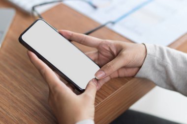 İki elinle ahşap masada ofis malzemelerini tutarak boş cep telefonu ekranını taklit et. 