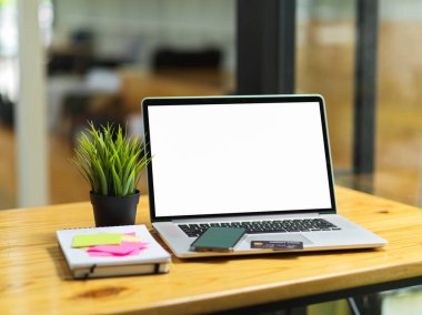 Portatif laptop boş ekran monitörü, akıllı telefon, kredi kartı, yapışkan notlar ve arka planda bulanıklık olan tahta masa üzerindeki diğer şeyler.