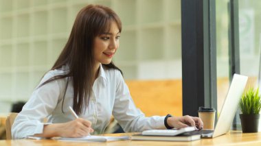 İşletme öğrencisi kütüphanede taşınabilir dizüstü bilgisayarla online ders veriyor, E-öğrenme konsepti, ev konseptinden çalışma