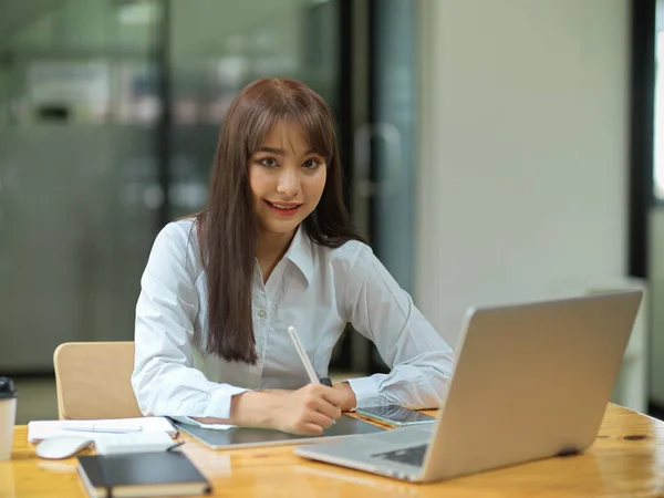 商界女性微笑着在平板电脑上工作 同时在办公室的木制桌子上拿着笔 笔记本电脑和文具 — 图库照片