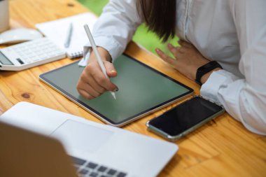 Kadın elinin kırpılmış görüntüsü, Stylus kaleminin yazısıyla akıllı telefon, dizüstü bilgisayar ve ahşap masa, kadın ders kitabı.