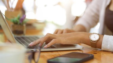 Dizüstü bilgisayarda yazan bir kadın, evden çalışan, kahve dükkanında, laptopta, akıllı telefonda ve ahşap masada gözlük takan resmi olmayan bir kadın resmi.